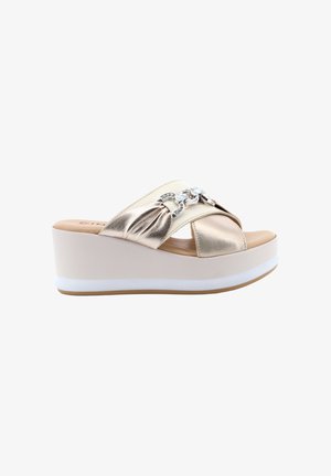 Sandalo con zeppa beige con cinturini incrociati in metallo oro e dettaglio decorativo con catena argento su sfondo bianco.