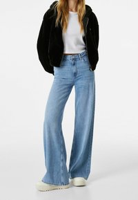 Svart fleece zip-up hoodie, vit kort t-shirt, högmidjade ljusblå vida jeans och beige plattformssneakers.