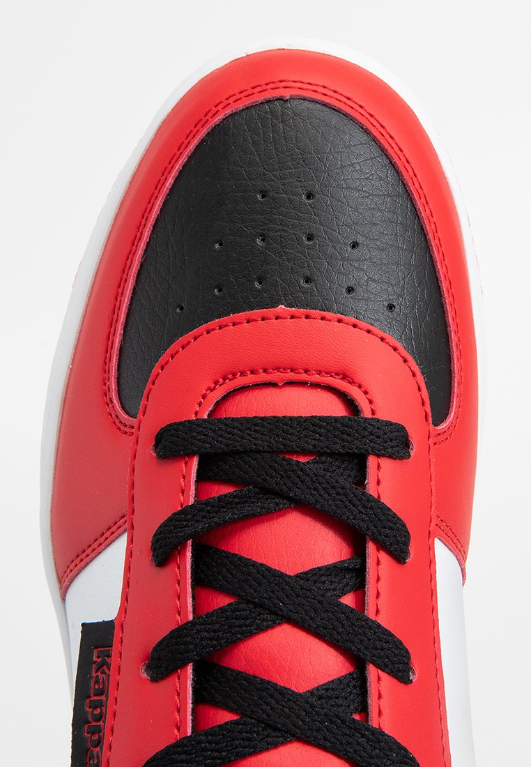 Zapatilla roja y negra con parte superior de cuero texturizado, cordones negros, cuello acolchado y suela de goma blanca. Presenta perforaciones en la punta.