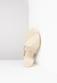 Sandalo in pelle marrone chiaro con suola in gomma beige, caratterizzato da una superficie liscia e testurizzata e dettagli sulle cinghie. Il logo del marchio è stampato sulla suola.