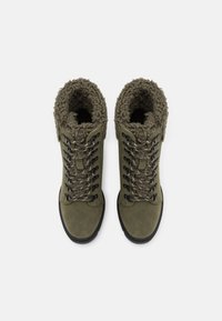 Oliwkowe zimowe buty z sztucznym futrem, czarną podeszwą i beżowo-czarnymi sznurówkami, pokazane z góry na białym tle.
