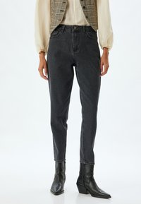 Zwarte high-waisted jeans met een taps toelopende pijp, zachte denimtextuur en minimale details. Gepaarde met een geruite vest en zwarte haklaarzen.