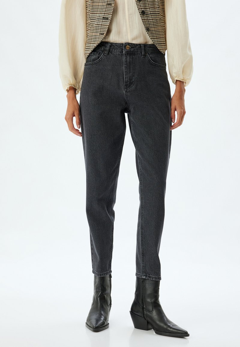 Zwarte high-waisted jeans met een taps toelopende pijp, zachte denimtextuur en minimale details. Gepaarde met een geruite vest en zwarte haklaarzen.