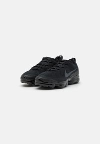 Black athletic shoes with a textured knit upper, lace-up design, and rounded black rubber sole. Features a subtle reflective logo on the side.