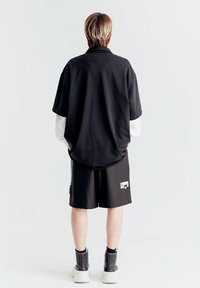 Camisa negra de gran tamaño con mangas largas blancas, combinada con pantalones cortos negros y botas negras hasta el tobillo. Presenta un corte relajado y un diseño simple.