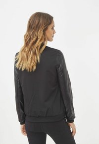 Chaqueta bomber negra con un cuerpo texturizado y mangas de cuero suave, con un dobladillo y puños acanalados para un ajuste ceñido.