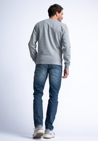 Szara bluzka z okrągłym dekoltem, z ribbingu na mankietach, noszona na niebieskich dżinsach. Swobodny krój uzupełniony jasnoszarymi trampkami. Prosty, funkcjonalny styl.