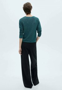 Turkusowy sweter dzianinowy z długimi rękawami, okrągłym dekoltem; zestawiony z czarnymi szerokimi spodniami. Prosty design, gładka tekstura, minimalne detale.