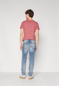 Röd kortärmad t-tröja med en melerad textur, kombinerad med ljusblå slim fit-jeans och beige sneakers, sett från baksidan.