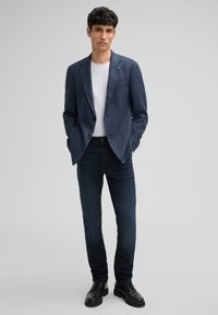 Granatowa marynarka w kratę z dwoma guzikami, noszona na białej koszuli, zestawiona z ciemnymi dżinsami i czarnymi butami, o dopasowanym kroju.