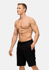 Pantaloni sportivi neri con cintura elastica e coulisse, dotati di tasche laterali e realizzati in un tessuto morbido e texturizzato.