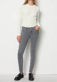 Housut vaaleanharmaata, kapeaa mallia, keskikorkealla vyötäröllä, valmistettu denimi-kankaasta. Yhdistetty tiukkaan valkoiseen ribattyyn pitkähiharaiseen puseroon ja mustiin paksupohjaisiin loafer-kengiin.