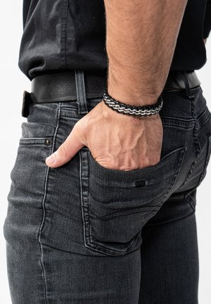 Black denim jeans with a slim fit, featuring subtle fading, five pockets, and a textured leather belt. Hand resting in the right pocket.