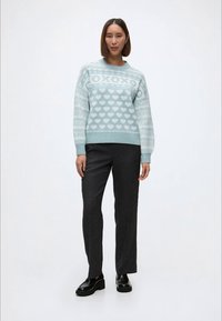 Gai zils džemperis ar sirds rakstiem, kombinēts ar tumši pelēkiem biksēm. Džemperim ir apaļa dekoltē un ribas rokturi. Melni zābaki.