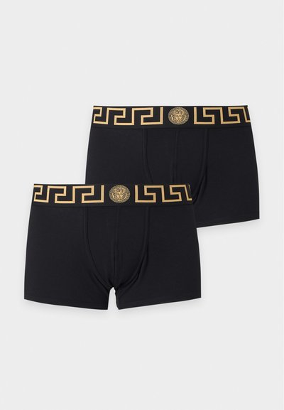 Deux boxers noirs avec un motif géométrique doré et un logo tête de Méduse sur des ceintures élastiques larges, affichés à plat sur un fond clair.