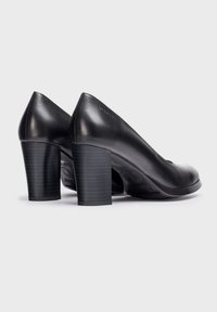 Zapatos de tacón alto de cuero negro con textura suave, punta redondeada y tacón grueso a rayas. Marca sutil en la parte trasera.