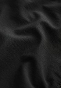 Schwarzer strukturierter Stoff mit einem dezenten karierten Muster, der sich weich legt und eine glatte Oberfläche aufweist. Lichtreflexionen heben die Textur hervor.