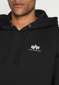 Felpa nera in misto cotone, con cappuccio regolabile, occhielli in metallo argento e logo bianco sul petto.