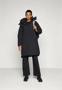 Schwarzer wasserdichter Mantel mit hohem Kragen, kombiniert mit passenden Hosen. Verfügt über eine lockere Passform, einen Reißverschluss vorne und große Seitentaschen.