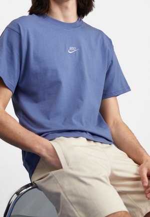 Krótki rękaw niebieska bawełniana koszulka z okrągłym dekoltem i małym białym logo Nike na piersi, w zestawie z beżowymi szortami.