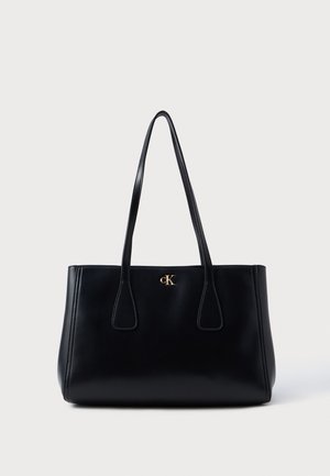 Svart skinn tote bag med to lange håndtak, featuring en gulllogo aksent på forsiden. Glatt tekstur og strukturert form.