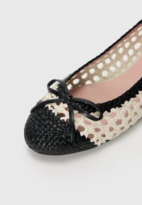 Ballerine en cuir tissé noir avec un design découpé crème, ornée d'un petit nœud noir sur le devant et d'une semelle intérieure rose pâle.