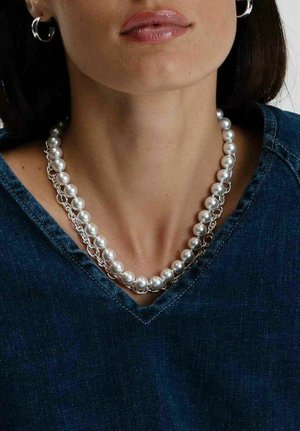 Pärlcollier med växlende stora och små pärlor, silverkedjeinslag, bärs över en denimtopp med V-ringning.