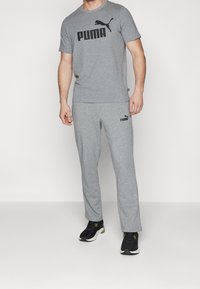 Grå sportsæt lavet af blød bomuld, bestående af en t-shirt med rund hals og et sort Puma-logo, parret med matchende bukser og sorte sneakers.