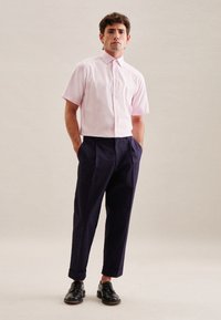Camicia rosa a maniche corte con bottoni abbinata a pantaloni navy scuri e scarpe di pelle nere. La camicia ha un colletto e una texture liscia.