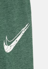 Πράσινες αθλητικές βερμούδες φτιαγμένες από υφή υφάσματος, με ένα μεγάλο λευκό λογότυπο Nike σε σχήμα σβησμένου που βρίσκεται στο αριστερό πόδι.