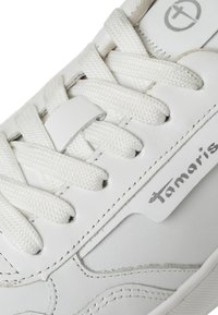 Chaussure de sport blanche avec un dessus en cuir lisse, des lacets texturés et un petit logo. Elle possède une semelle rembourrée et des accents cousus.