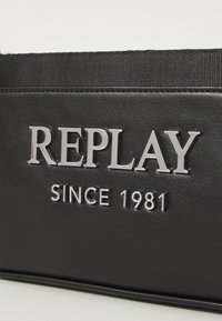Borsa in finta pelle nera con superficie testurizzata, logo argentato in rilievo "REPLAY" e "SINCE 1981" in testo argentato più piccolo.