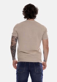 Maglione corto a maniche corte beige a coste con un design aderente, tessuto testurizzato e scollo rotondo, abbinato a jeans in denim blu scuro.