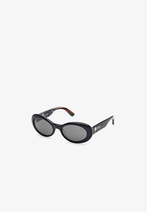 Gafas de sol negras con lentes ovalados, tinte gris oscuro y acabado brillante. Las patillas presentan un patrón multicolor y un detalle del logo en dorado.