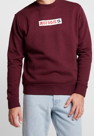 Felpa bordeaux realizzata in morbido tessuto, con una toppa rettangolare bianca con la scritta "JUST DO IT." in rosso e un logo, polsini e orlo a coste.