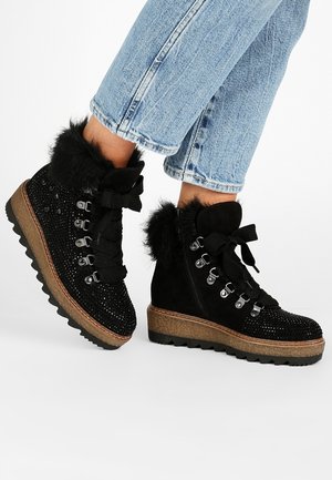 Botas negras hasta el tobillo con ribetes de pelo sintético, cordones decorativos y acentos de strass, combinadas con jeans azul claro con remangue.