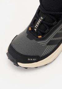 Svart og grå atletisk sko med en teksturert overdel, gummisåle og RAIN.RDY-merke. Har geometriske mønstre og en polstret design.