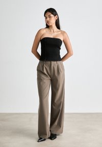 Μαύρη strapless τοπάκι από τζιν; ψηλόμεσο, ανοιχτό καφέ παντελόνι με πλευρική κουμπότρυπα; μαύρα γόβες με αιχμηρή μύτη. Απλός φόντος.