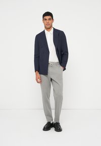 Μπλε διπλόκουμπο σακάκι, λευκό πουκάμισο με γιακά, γκρι παντελόνι με κορδόνι και μαύρα παπούτσια. Απλός σχεδιασμός, λείος υφασμάτινος, ραμμένη εφαρμογή.