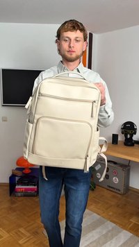 Mochila de tom bege claro, feita de material suave, com múltiplos compartimentos com fechos éclair, um bolso frontal e alças ajustáveis.