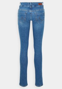 Jean slim bleu avec poches arrière, coutures marron et petite étiquette en cuir de la marque sur la ceinture.