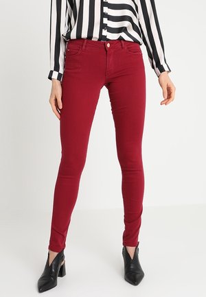 Pantalones rojos ajustados combinados con una camisa de rayas verticales en blanco y negro y botines negros con tacón.