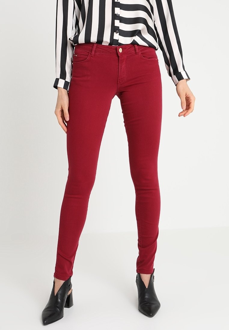 Pantalon rouge slim associé à une chemise rayée verticale noire et blanche et des bottines noires à talons.