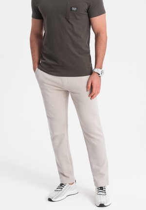 Světlé šedé slim-fit kalhoty s přední kapsou, v kombinaci s tmavým tričkem s krátkým rukávem a bílými síťovanými teniskami. Jednoduchý, neformální design.