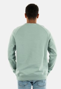 Sudadera verde menta con mangas raglán, puños y dobladillo acanalados, hecha de una tela suave y texturizada, combinada con jeans azul claro.