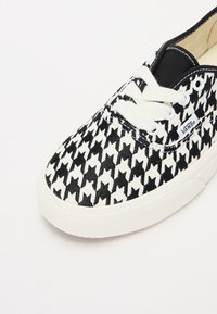 Kangas ketsid musta ja valge houndstooth mustriga, valged paelad ning mustad aktsendid põlle ja silmade ümber. Kummitald.