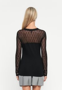 Long-sleeve top featuring a sheer patterned black mesh design on sleeves and back, with a solid black body and rounded neckline.