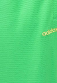 Zelená sieťovina z dresového materiálu s textúrovaným povrchom. Obsahuje malé zlaté logo "adidas" na boku. Jednoduchý a športový dizajn.