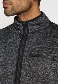 Πλεκτό μπουφάν με φερμουάρ σε σκούρο γκρι χρώμα με υφή μοτίβο, διαθέτει μαύρο φερμουάρ και τσέπη στο στήθος με κλείσιμο με φερμουάρ.