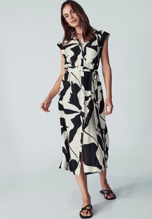Maxi šaty v béžové barvě s černými abstraktními vzory, krátkými rukávy, přední kapsou a pásem v pase. Hladká látka s postranními rozparky.